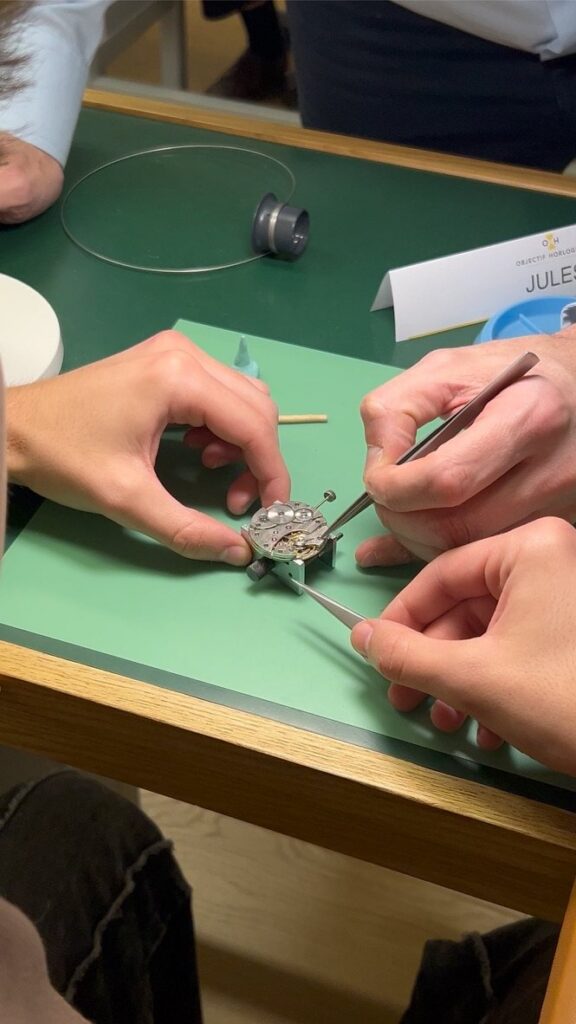 Atelier avec Objectif Horlogerie Mains manipulant un mouvement à la pince, pendant l'atelier Objectif Horlogerie