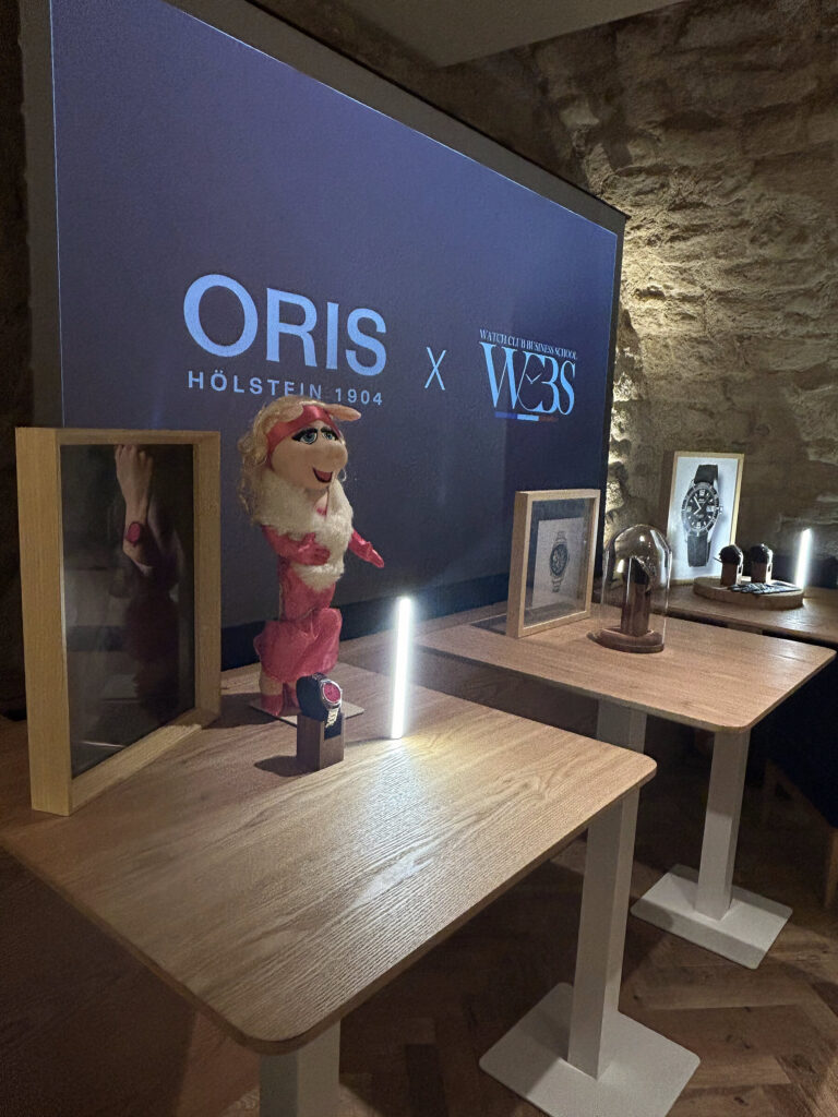 &Eacute;cran Oris &times; WCBS et figurine de Miss Piggy pr&egrave;s des montres expos&eacute;es