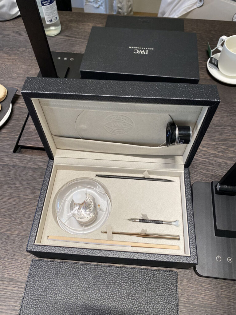 Coffret d'atelier IWC ouvert : mouvement, outils et gants posés sur la table